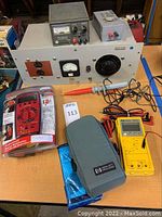Overview of all items on table showing the vintage HP external power supply, power stat with analog voltmeter and current and resistance box, Ansmann digital multimeter in packaging, and yellow HP digital multimeter with grey carrying case and leads.