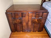 Front view of walnut nightstand showing geometric carved door panels and overall finish