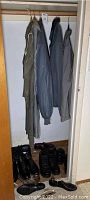 Four jackets hanging in closet with shoes arranged beneath them; includes military trench coat, Columbia jacket, fleece zip-up, plus one more jacket