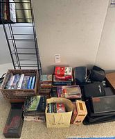 Overview of recorded media lot showing cassette tapes, VHS tapes including blank tapes, DVDs, CDs, storage boxes and carry cases, and media rack against a beige wall.