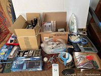Top-down view of multiple personal care items spread on a textile surface including Rowenta iron, digital scale, grooming tools, and packaging boxes.