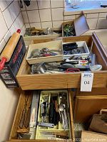 Drawer filled with assorted kitchen utensils including rolling pin, tongs, measuring spoons, wine bottle openers, and other tools.
