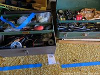 Two steel toolboxes filled with assorted hand tools, hardware, wires, and accessories including pliers, spools of wire, and sanding attachments.