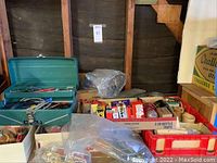 Photo showing green metal tool box open with various electronic tools inside, surrounded by plastic trays containing wires, boxes, and electronic supplies.