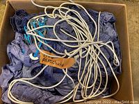 Top view of blue silk parachute fabric with coiled white ropes and attached metal washers inside a cardboard box.