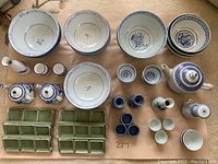 Top-down view of the entire dish set including blue and white bowls, teapots, small cups, and green divided trays arranged on a beige surface.