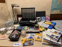 Front view of the Canon printer surrounded by various stationery, photo papers, desk lamp, keychains, and office supplies on a table.