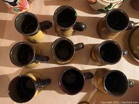 Overhead view of 9 pottery beer stein mugs with dark handles and interiors, yellow and brown earthy glaze