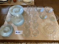 Full set of frosted glassware laid out on a table including plates, bowls, and mugs, all with floral pattern.