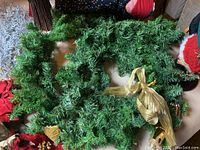 Green artificial Christmas garland with a gold bow, lying on a surface with other decorations around it.