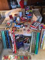 Wide view of the large lot showing wrapping paper, gift bags, gift boxes, ribbons, tags, and tins displayed on a couch and floor.