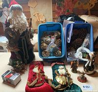 Photo showing large Santa figure, two Christmas stockings, snowman and angel figurines, pinecones in bags, and blue bins.