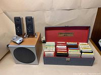 Full view of Logitech speakers, subwoofer, control unit, and open box of 8-track tapes showing contents