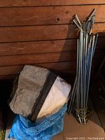 Folded canopy fabric and blue plastic wrapping against a wooden wall