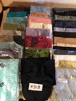 Display of 26 assorted pashminas arranged in rows showing different colors and patterns, some still in plastic packaging.