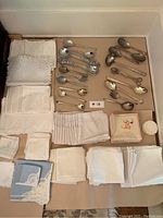 Full display of assorted serving spoons, forks, and various napkins and place mats laid out on table