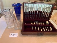 Cutlery set with knives and other flatware in wooden case and three different glass vases beside the case.