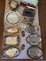 Full lot overview of silver plated trays, candle sticks, steak knives in box, and serving pot arranged on a flat surface.