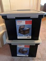 Front view of two stacked Storex file totes with gray lids and black bodies, showing the label indicating they are Staples Portable File Totes.
