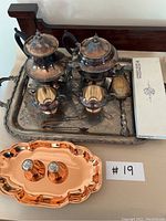 Overall shot of the silver plated copper tea set on ornate serving tray plus copper salt and pepper shakers on a copper tray.