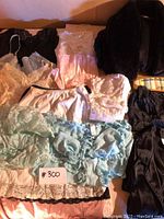 Photo showing a variety of lingerie items laid out including white, pink, and blue slips, camisoles with lace, and a black plush robe and black PJ set.