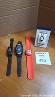 Four watches laid out on wooden surface with brown cardboard background: black sport smart watch, black digital 'spy' watch, red snap wrist band Canada watch, TimeZone wristwatch in box.