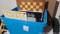 Photo showing exterior of blue plastic bin full of games and puzzles including a wooden chess/checkerboard and alphabet learning cards