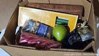 Box containing various candles, a carved wooden candle holder, pebble-filled glass candle holders and a green apple shaped candle.
