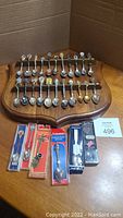 Wide view of 28 collector spoons on wooden display stand and 6 spoons in packaging.