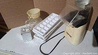 Photo of vintage popcorn machine, toaster, glass jug, funnel, ice cube trays, and candle holder on white surface.