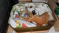 Top view of the assorted salt and pepper shakers including rabbit with nest, fox figure, beer stein, and other figurines inside a metal tin box with tissue paper
