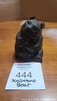 Front view of small black soapstone bear figurine sitting on surface with label in front.