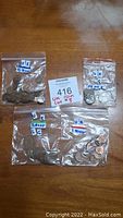 Five plastic zip bags containing various UK coins labeled by denomination placed on wooden surface with MaxSold tag visible.