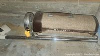 Side view of vintage Electrolux cylinder vacuum showing brown textured body and metallic chrome wand with white floor nozzle nearby
