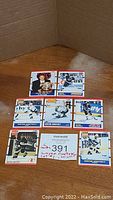 Six Wayne Gretzky hockey cards arranged on a wooden surface inside a cardboard box. Cards include various images of Gretzky in action and posed, showcasing different card designs and manufacturers visible such as O-Pee-Chee and Pro Set.