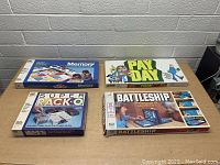 Four vintage board games on a table against a brick wall including PayDay, Battleship, Memory, and Super Racko in original boxes.
