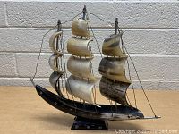 Front view of vintage steer/bovine horn carved ship sculpture showing three masts with sails and rigging, mounted on a pedestal base.