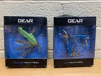 Two Travel Gear multi-tools in original packaging, showing front of boxes behind clear plastic. One green Deluxe model and one blue LED model.