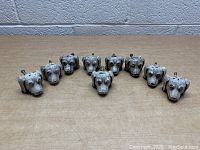 Lot of nine metal dog head cabinet/drawer pull knobs arranged side by side revealing sculpted facial details and silver-tone finish.