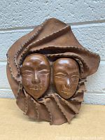 Front view of tan leather sculpture showing two faces and detailed leather folds