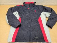 Front view of navy blue boys Spyder winter jacket with red and gray accents laid flat on table.