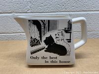 Front view of the square-shaped ceramic jug showing the black and white illustration of two dogs by a fireplace with the caption "Only the best in this house"