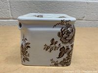 Side view of square ceramic tea pot showing brown floral design and spout