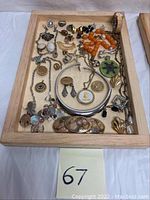 Overhead view of wooden tray containing assorted costume jewelry including necklaces, bracelets, earrings, pendants, and a wristwatch.