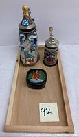 Photo of two German beer steins and a lacquered box arranged on a wooden tray.