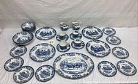 Full set laid out on white cloth showing platters, plates, creamer, cups, and bowls with Coaching Scene pattern in blue and white