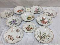 Shot of ten Limoges France porcelain plates arranged showing floral designs and scalloped gold rim edges.