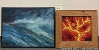 Two abstract paintings side by side on the floor; one ocean wave scene with black frame, one red/orange branching abstract with wooden frame.