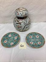 Ginger jar with lid and two turquoise decorative plates with Chinese symbols, arranged on white background.