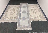 Three wool rugs laid out on floor: two rectangular area rugs and one narrow runner in center. Rugs have carved floral and geometric designs in pastel colors with fringes on ends.